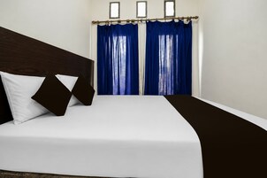 Una habitación de hotel con una cama, ropa de cama blanca, un cabecero oscuro y cortinas azules.