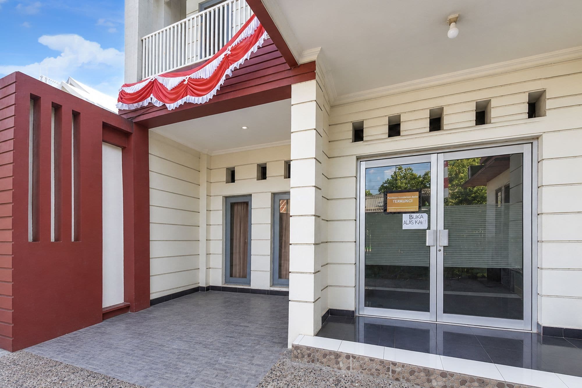 A building with a red and white facade, a glass door entrance, and a small balcony with a red awning.