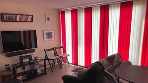 A living room with a flat-screen TV, a sofa, a dining table with chairs, and a bookshelf. - Attractive apartment which has, possibly,  the best views in Felixstowe (Felixstowe)