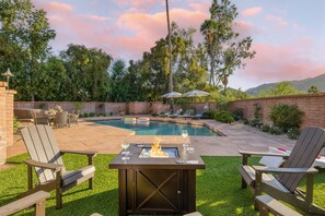 A backyard with a pool, outdoor seating, and a fire pit.