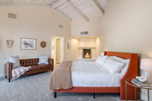 Une chambre à coucher avec un lit, un canapé, une cheminée et une petite table avec une lampe.
