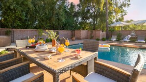 An outdoor dining area with wicker furniture, a pool, and lounge chairs. - Pool, Firepit Lounge, Cornhole, and Outdoor Kitchen + Dining Area | Diamondback (Scottsdale)