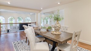A dining area with a wooden table, white upholstered chairs, and a decorative vase. - Pool, Firepit Lounge, Cornhole, and Outdoor Kitchen + Dining Area | Diamondback (Scottsdale)