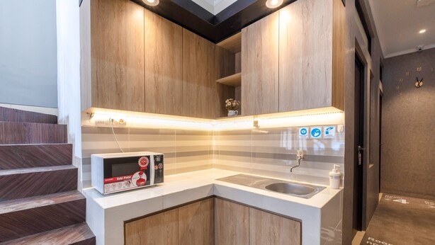 A modern kitchen with wooden cabinets, a built-in sink, and a countertop with a box of Koi Paint. - OYO Life 3246 Walnut Inn G-10 (Karawang)