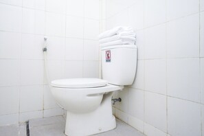 A white toilet with a no smoking sign on the tank, a white tiled wall, and a small trash bin to the left. - OYO Life 3246 Walnut Inn G-10 (Karawang)