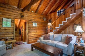 A log cabin interior with a sofa, coffee table, staircase, and wooden walls.