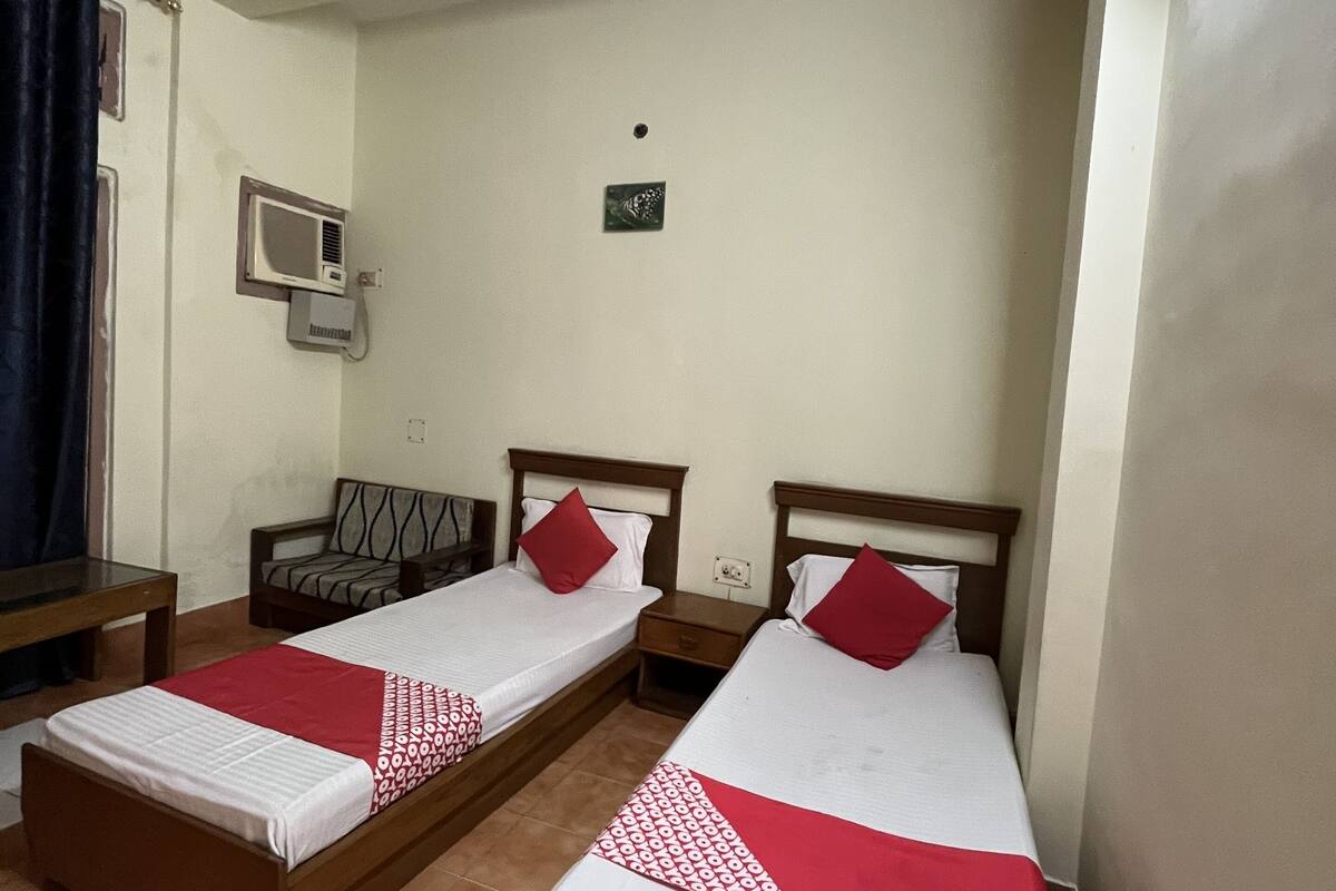 A room with two single beds, a ceiling fan, a small air conditioning unit, and a window with curtains.