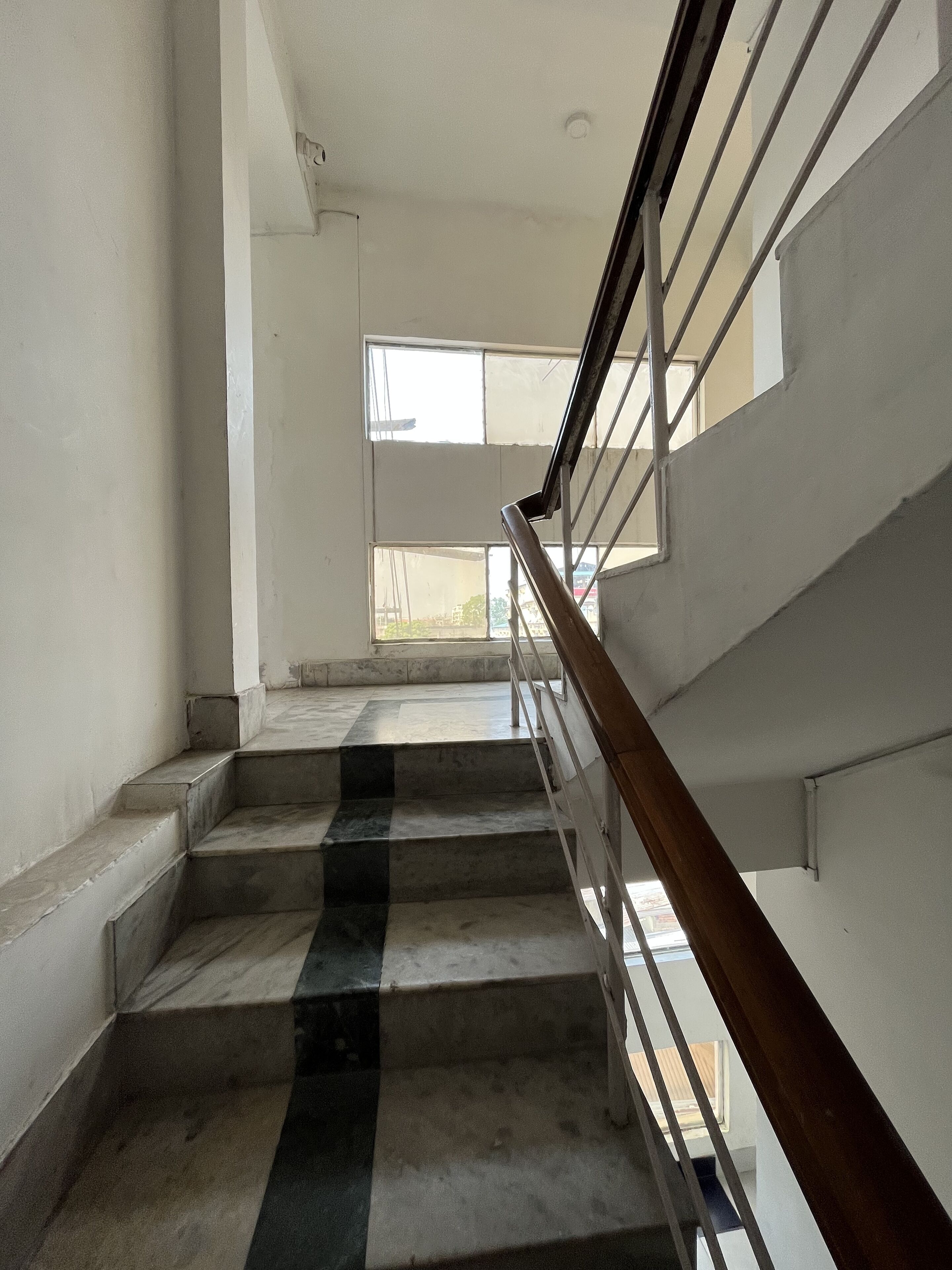 Un escalier avec une main courante en bois et des balustres en métal, menant à un palier doté d’une grande fenêtre.