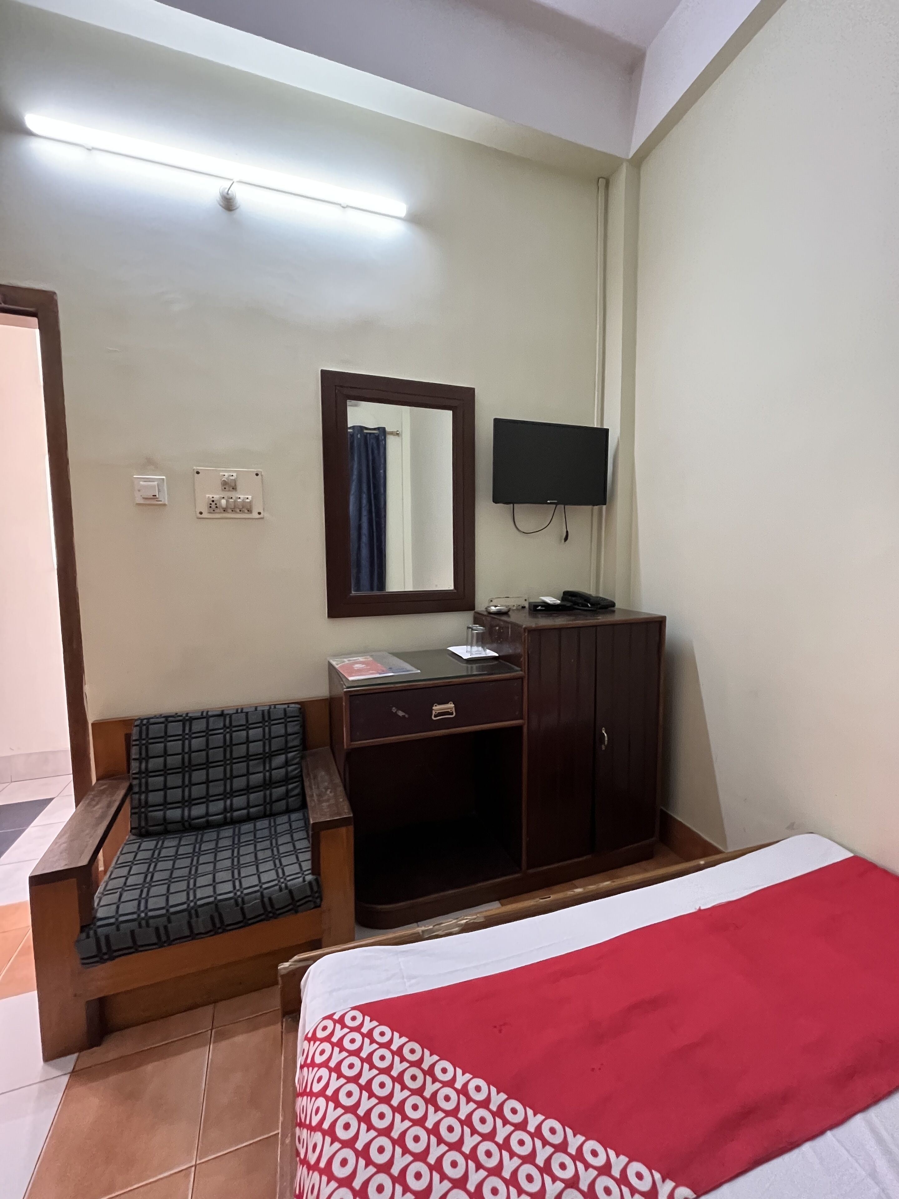 A hotel room with a bed, a sofa, a desk with a mirror, a television, and a wardrobe.