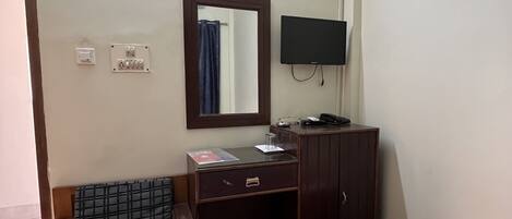 A hotel room with a bed, a sofa, a desk with a mirror, a television, and a wardrobe.