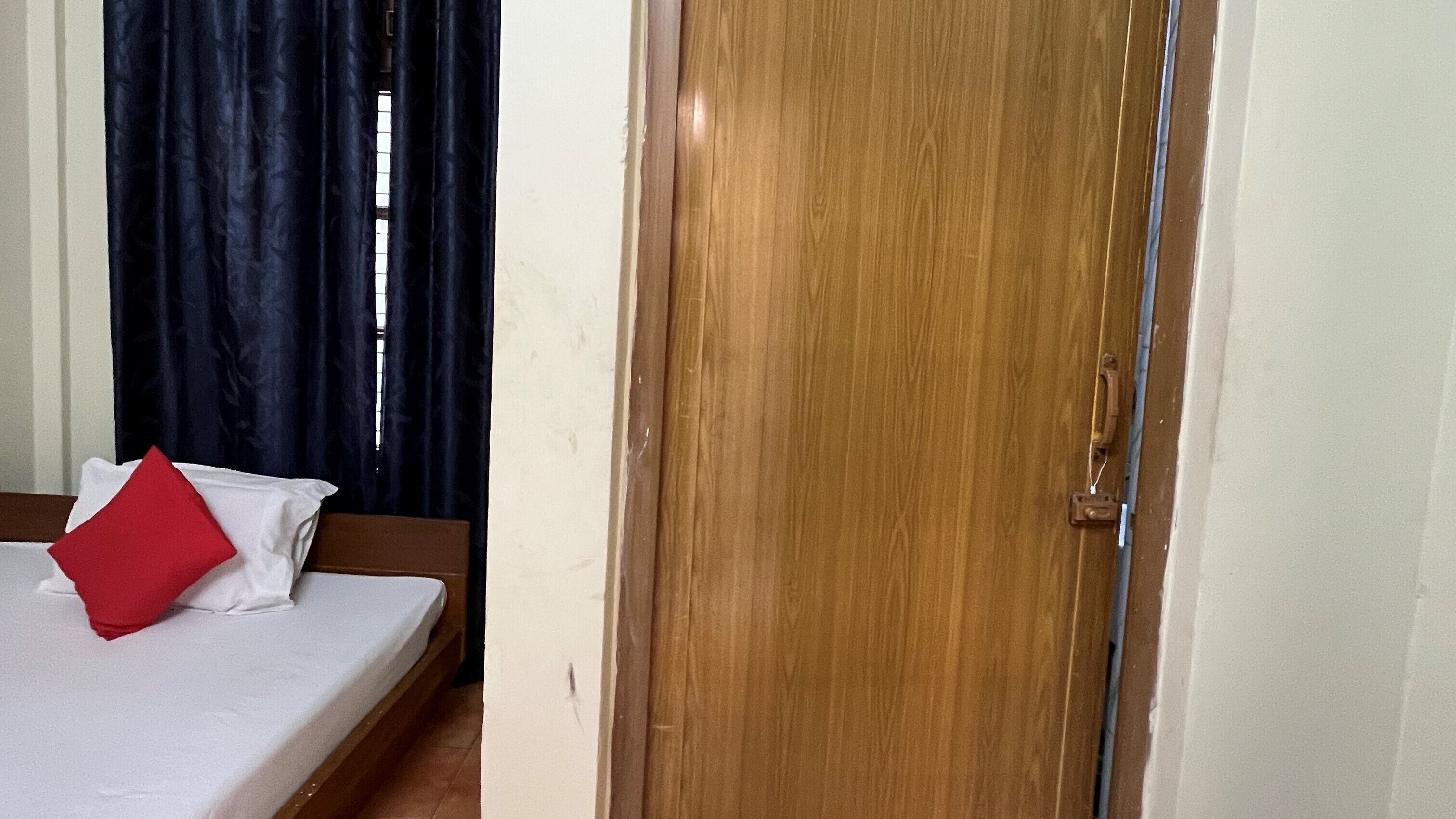 A room with a bed, a wooden door, and a window with curtains.