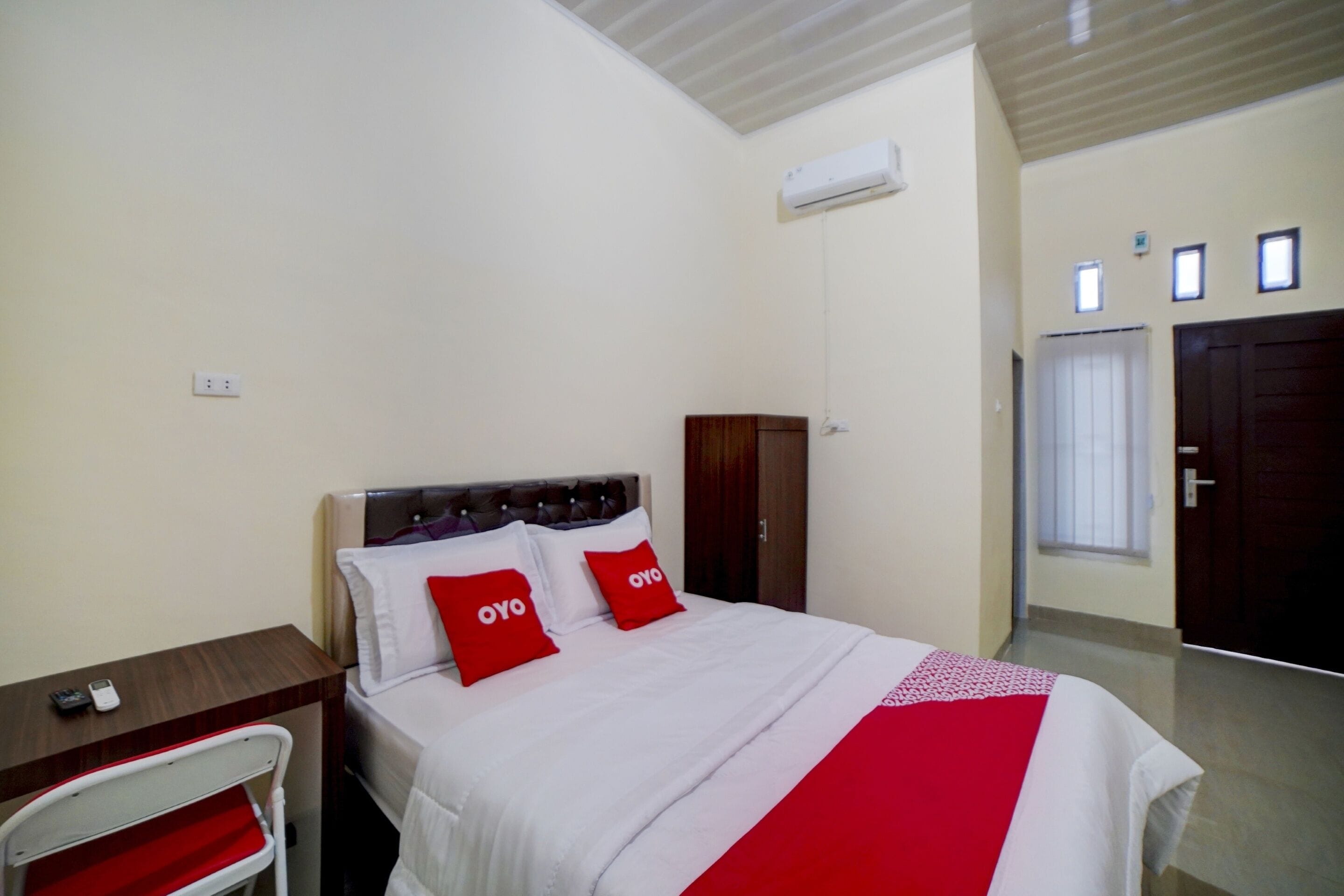 A hotel room with a bed, a desk, a chair, a wardrobe, and an air conditioning unit.