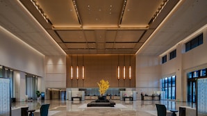 A spacious lobby with a central reception desk, modern lighting, and a polished marble floor.