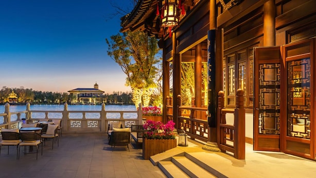 A traditional Chinese-style building with a wooden exterior, a balcony with seating, and a view of a body of water in the background.