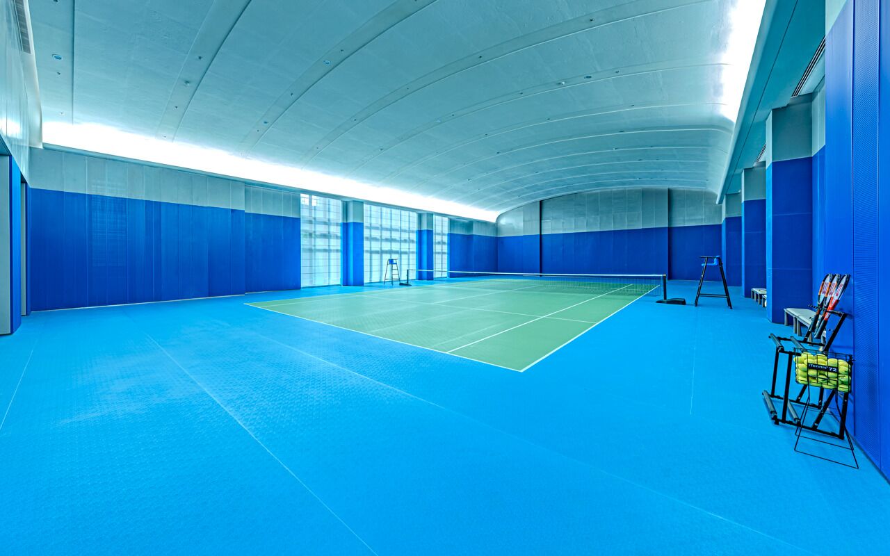 An indoor tennis court with blue walls and a green playing surface.