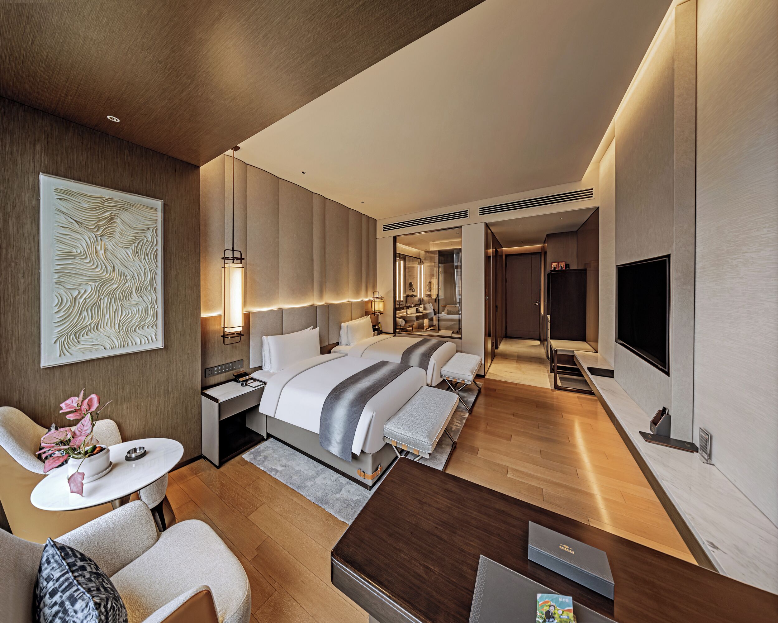 A modern hotel room with a large bed, a desk, a TV, and a bathroom visible through an open door.