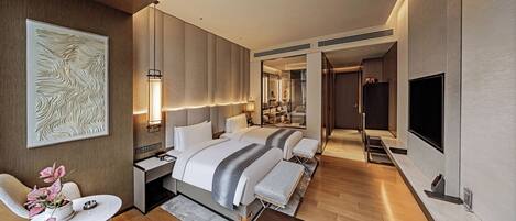 A modern hotel room with a large bed, a desk, a TV, and a bathroom visible through an open door.