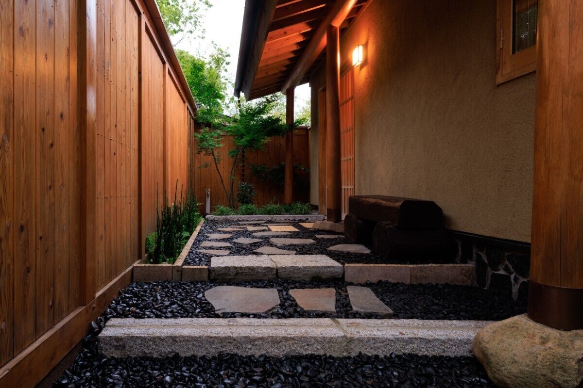 A wooden pathway leading to a covered seating area with a stone-tiled ground.