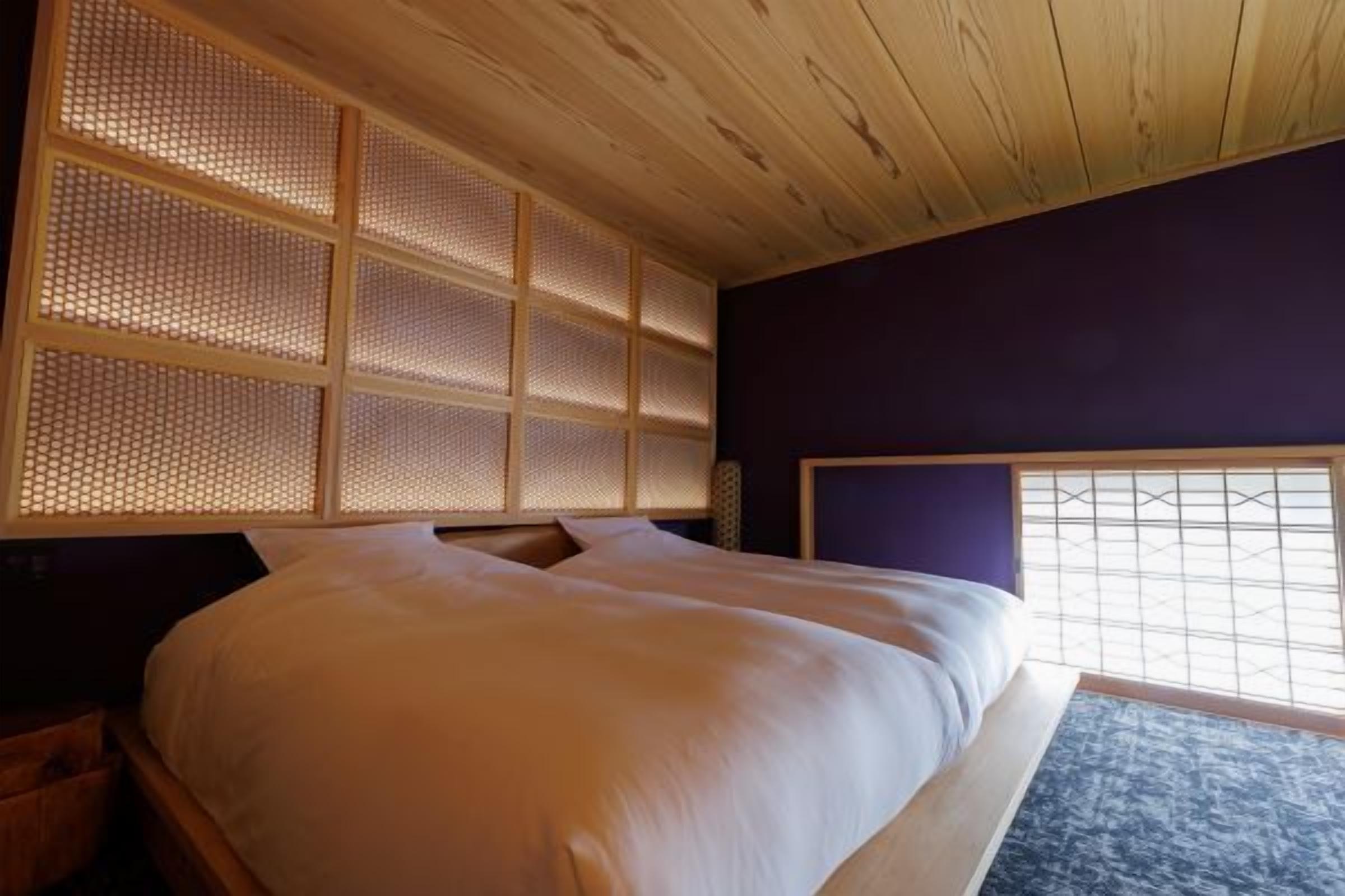 A room with a bed, wooden ceiling, and a window with a grid pattern.