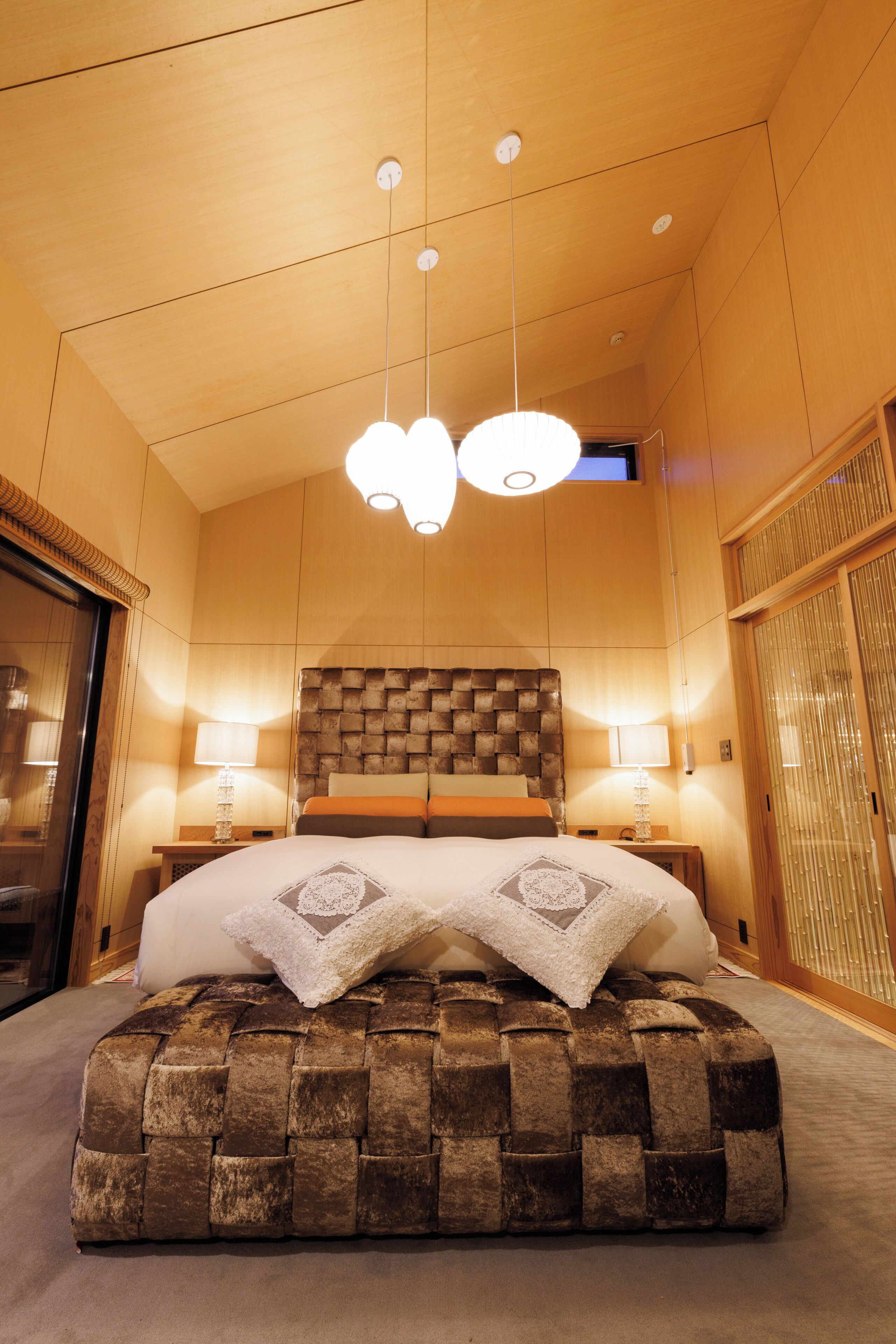 Ein Hotelzimmer mit einem großen Bett, einem gewobenen Ottomanen, zwei Nachttischlampen und einer Deckenleuchte.