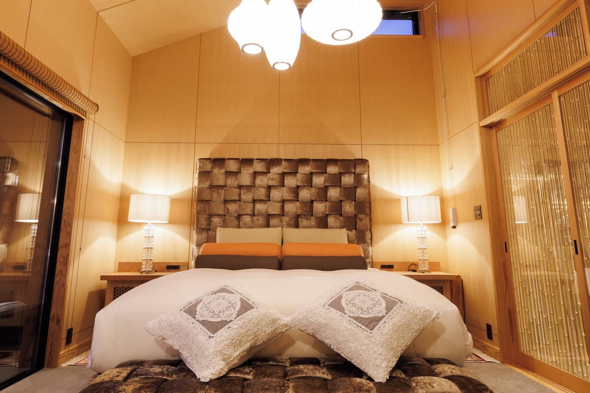 A hotel room with a large bed, a woven ottoman, two bedside lamps, and a ceiling light fixture.