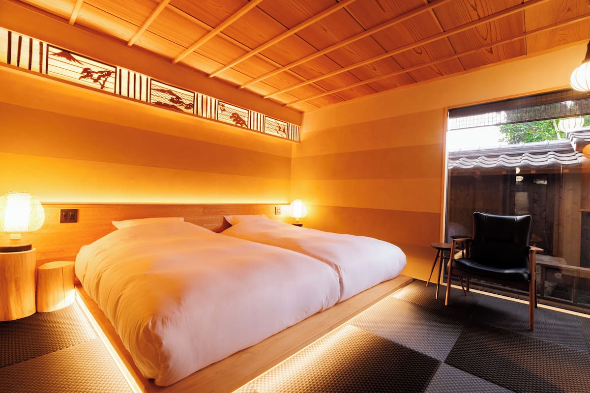 A hotel room with a large bed, two bedside lamps, a chair, and a view of the outside through a glass door.