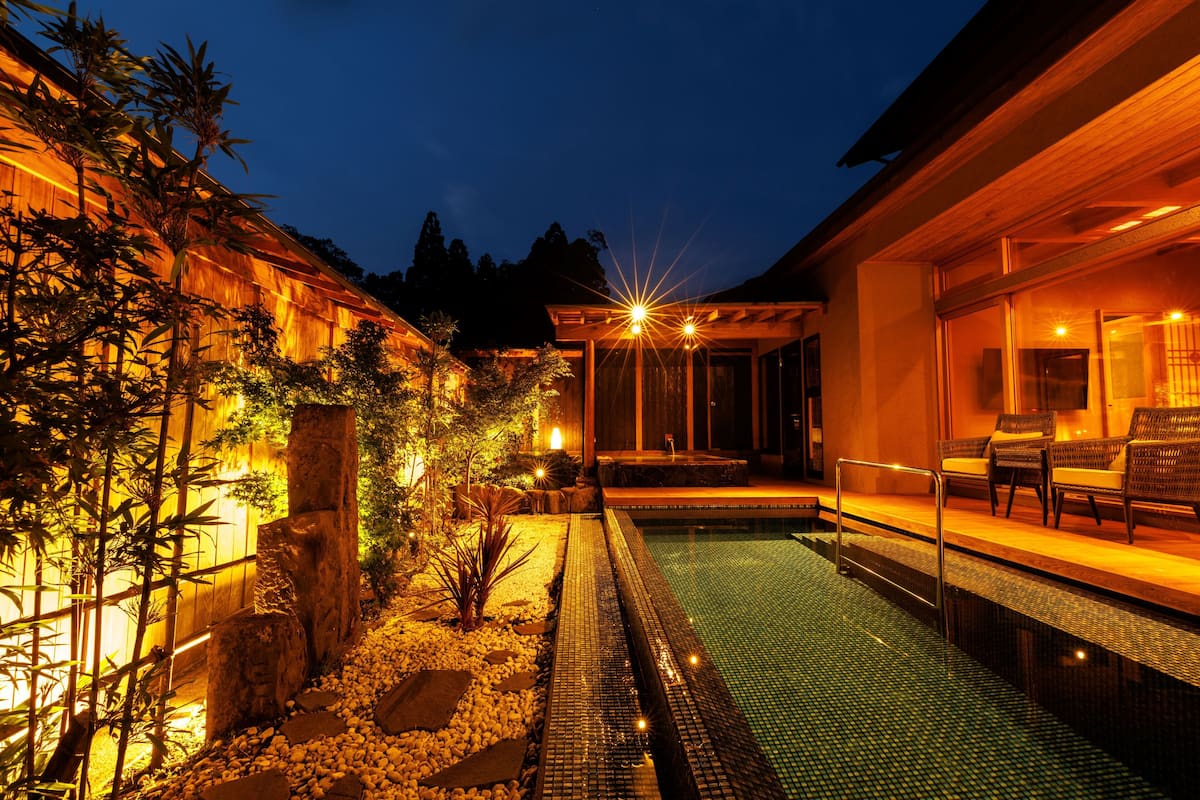 A swimming pool with a tiled deck, surrounded by a wooden deck and a garden with rocks and plants.