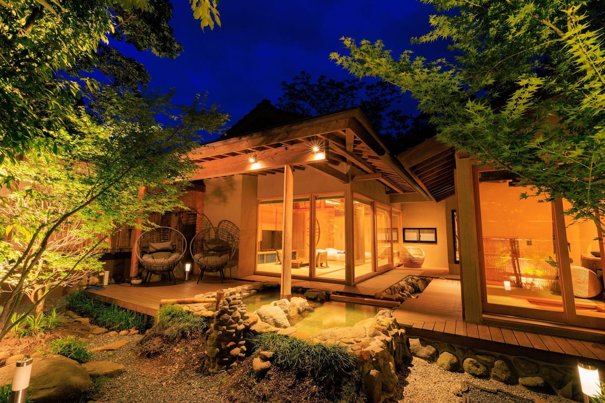 A modern house with a wooden deck, a koi pond, and a glass-enclosed patio area.