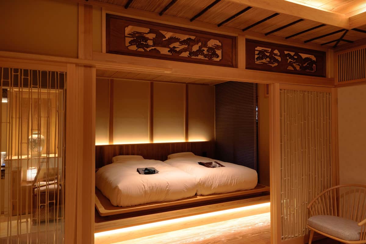 A traditional Japanese-style bedroom with a low platform bed, sliding doors, and a wooden ceiling.
