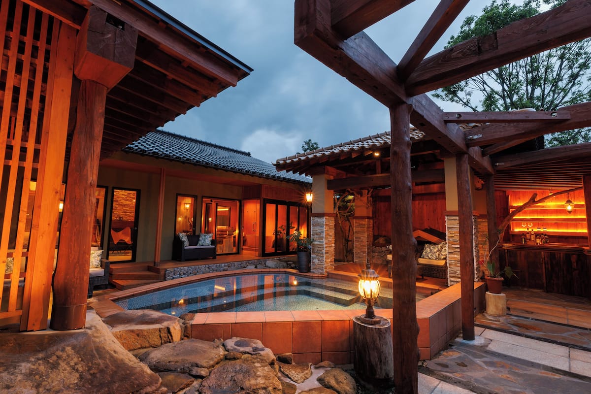 A pool area with a stone border, wooden pergola, and a seating area with a view of the pool.