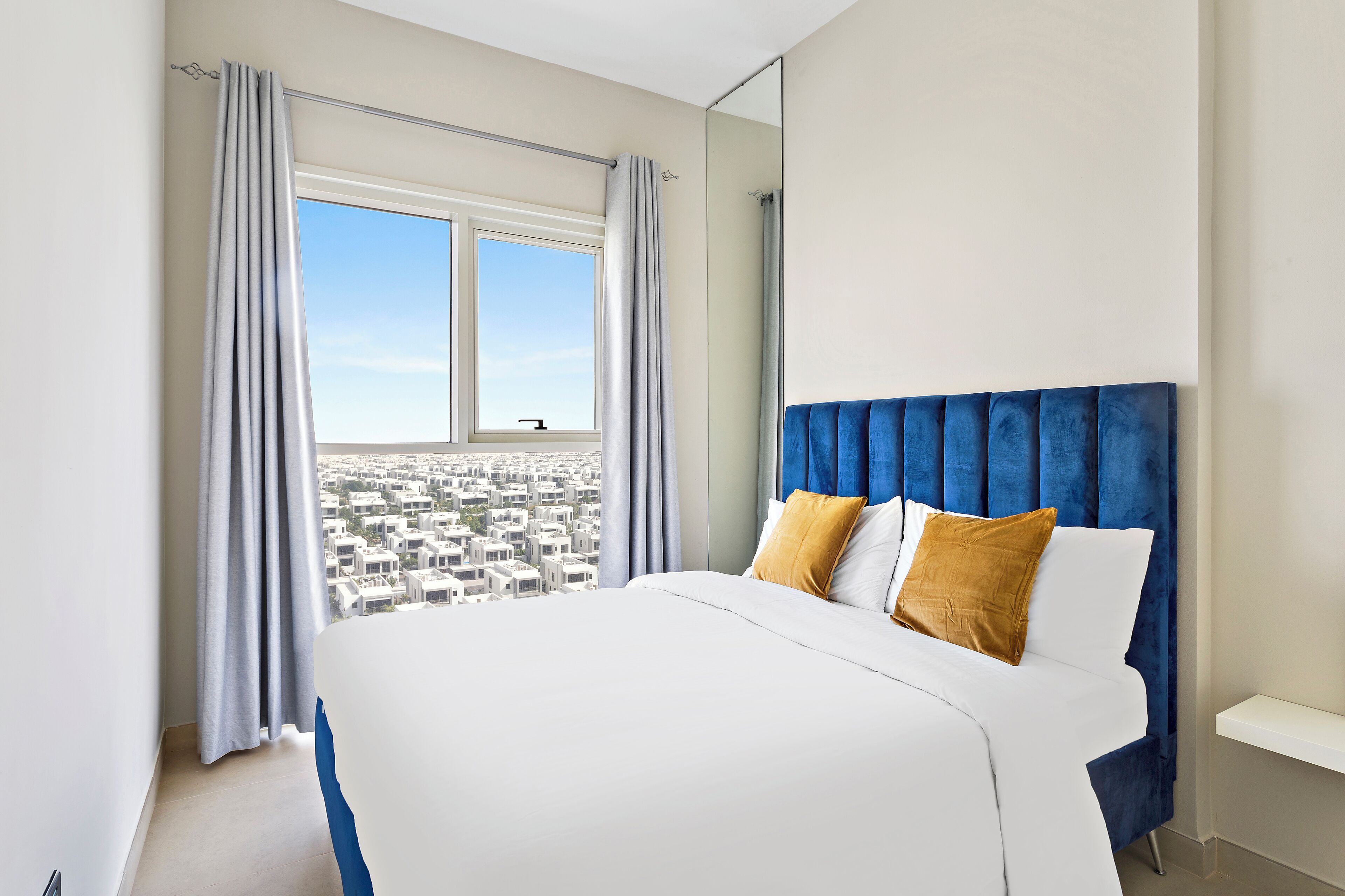 A hotel room with a large bed, a view of the city, and a blue headboard.