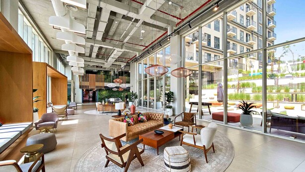 Eine großzügige Lobby mit modernem Design, ausgestattet mit einer zentralen Sitzecke mit Sofas und Sesseln, großen Fenstern mit Blick auf die Stadt und einer hohen Decke mit freiliegenden Balken und Leuchten.
