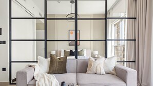 Ein modernes Wohnzimmer mit einem grauen Sofa, einem Holztisch und einem spiegelnden Wandbild mit schwarzem Rahmen.
