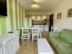 Una sala de estar con un sofá verde, una mesa de centro blanca y un comedor con una mesa y sillas blancas.