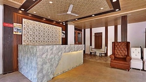 A reception area with a marble counter, a patterned wall, a ceiling fan, and a brown leather chair. - The Neer Budha (Narendranagar)