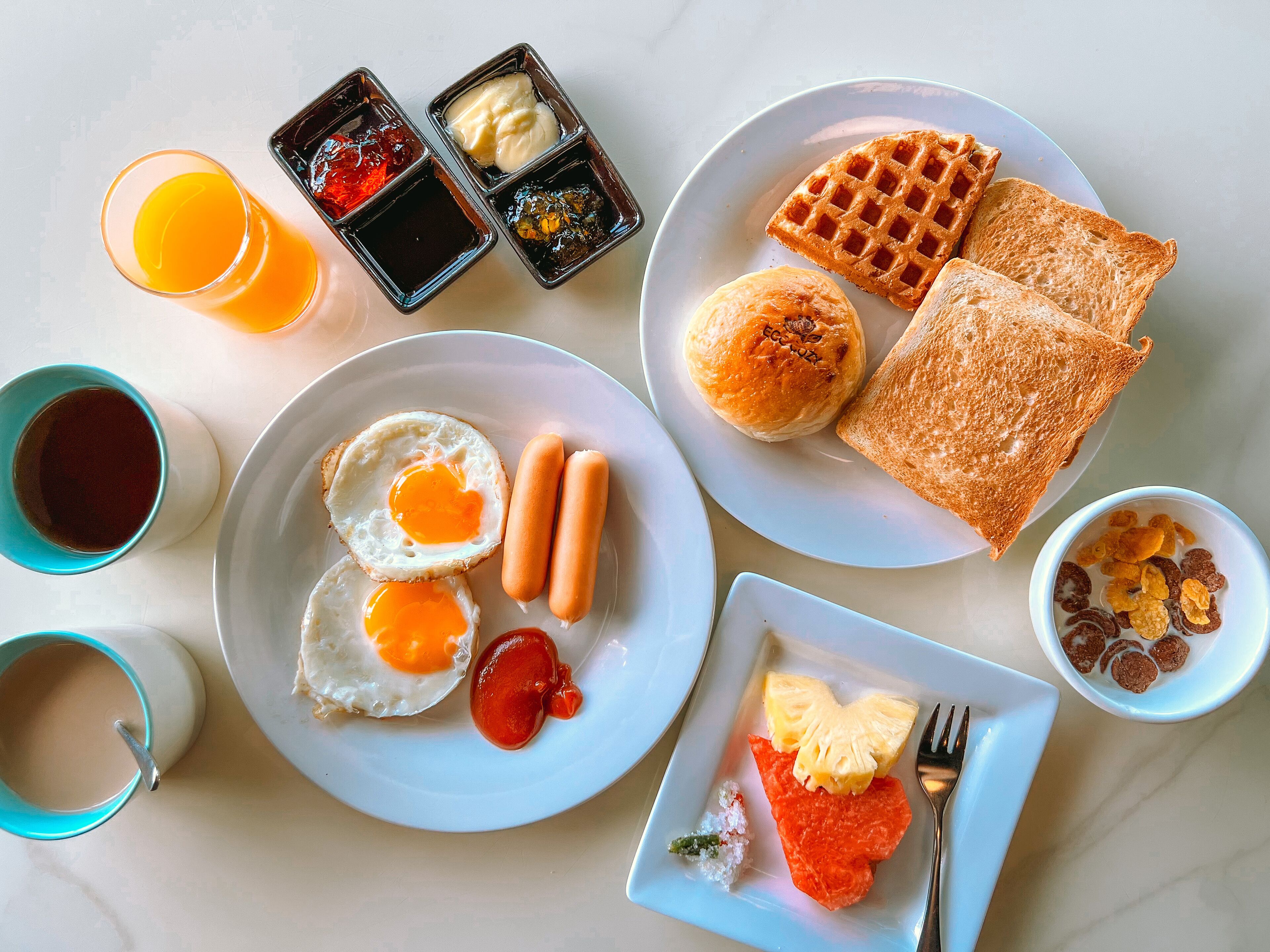A breakfast spread with eggs, sausages, toast, waffles, and various condiments on plates.