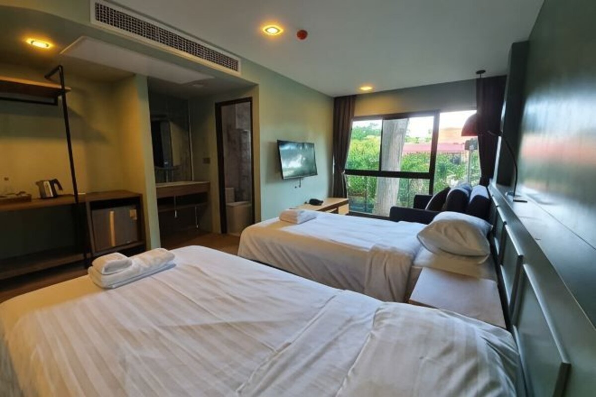 A hotel room with two beds, a TV, a desk, and a window with a view.