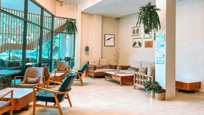 A spacious lobby with modern furniture, large windows offering a view of the outdoors, and various amenities like a reception desk and wall-mounted signs. - Eco Cozy Beachfront Resort Chaam (Cha-am)
