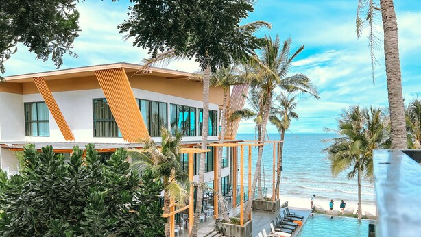 A modern hotel with a pool, palm trees, and a view of the ocean. - Eco Cozy Beachfront Resort Chaam (Cha-am)