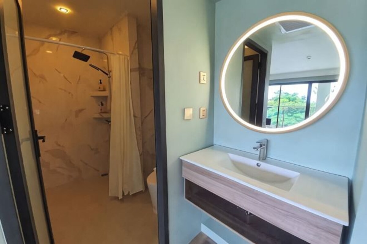 A bathroom with a modern vanity, a round mirror, and a shower area.