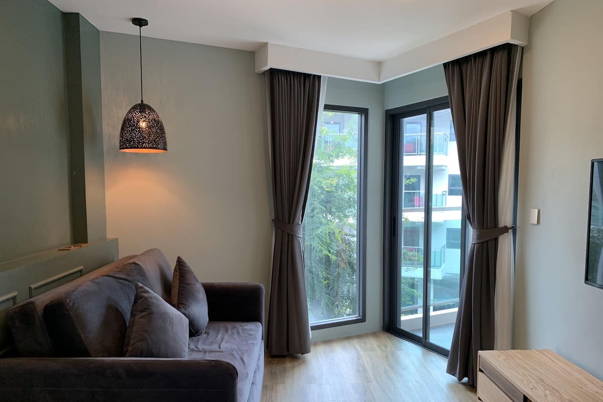 Un salon moderne avec un canapé de couleur foncée, un luminaire suspendu et de grandes fenêtres ornées de rideaux.