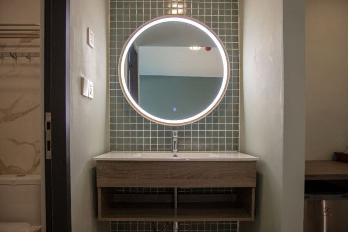 A bathroom with a round mirror, a sink, and a tiled backsplash.