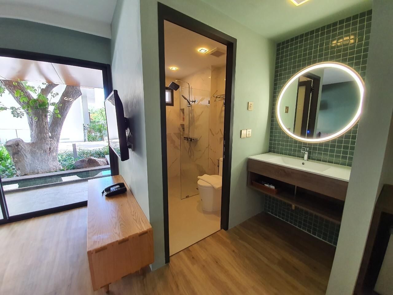 A modern bathroom with a wooden vanity, a glass shower enclosure, and a mirror with a light.