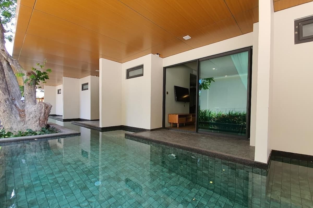 Un espace piscine intérieur moderne, avec une eau d’un bleu limpide, un plafond en bois et un banc près de la porte vitrée.