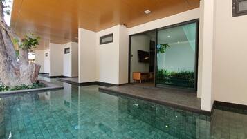 Un área de piscina interior moderna con agua azul cristalina, techo de madera y un banco cerca de la puerta de cristal.