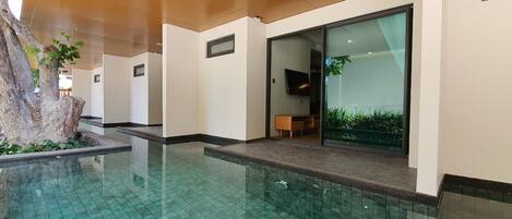 Un área de piscina interior moderna con agua azul cristalina, techo de madera y un banco cerca de la puerta de cristal.