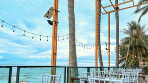 An outdoor dining area with tables and chairs, overlooking the ocean, with string lights and palm trees. - Eco Cozy Beachfront Resort Chaam (Cha-am)