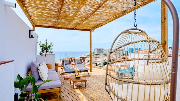 Une terrasse en bois avec deux chaises longues, un fauteuil suspendu et une petite table sur laquelle se trouve un saladier rempli de fruits.