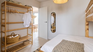Une chambre avec une armoire en bois, un lit avec une literie à motifs, un luminaire suspendu et un miroir au mur.
