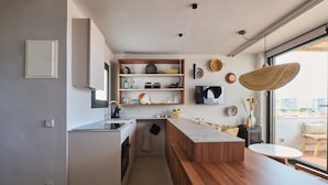 Une cuisine moderne dotée d’un îlot central en bois, d’étagères intégrées et d’une grande fenêtre offrant une vue sur la ville.